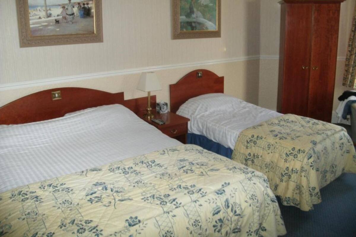A hotel room with two beds, a wooden wardrobe, and two framed pictures on the wall.