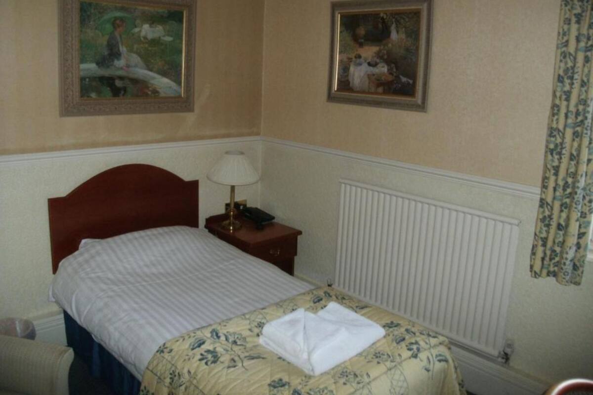 A hotel room with a bed, a nightstand with a lamp, and two framed paintings on the wall.