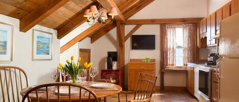 A cozy kitchen with wooden beams, a dining table with chairs, a refrigerator, and a window with curtains.