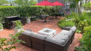 A patio with a wicker sofa, a fire pit, and a red umbrella. - Seven Sea Street Inn (Nantucket)