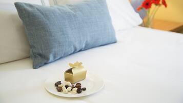 A neatly made bed with a blue pillow, a small gift box, and a plate of chocolates.