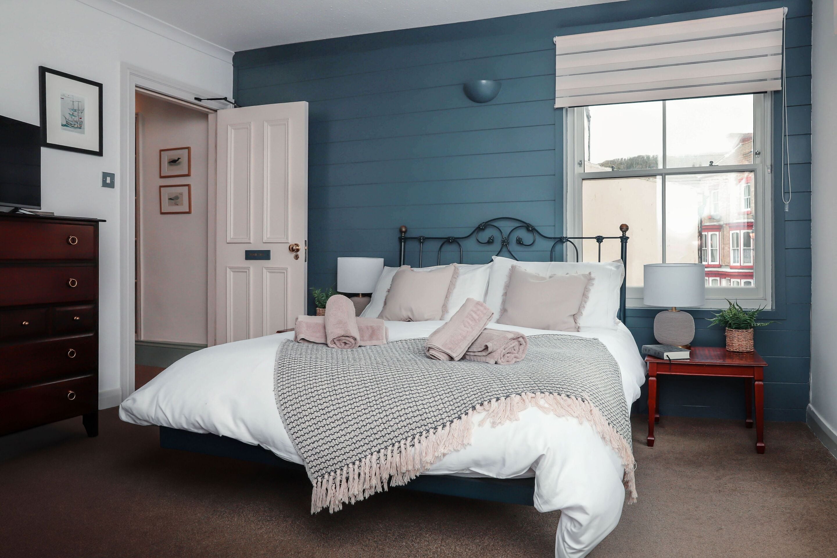 A bedroom with a bed, bedside tables, a dresser, and a window with a view of buildings.
