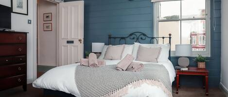 A bedroom with a bed, bedside tables, a dresser, and a window with a view of buildings.
