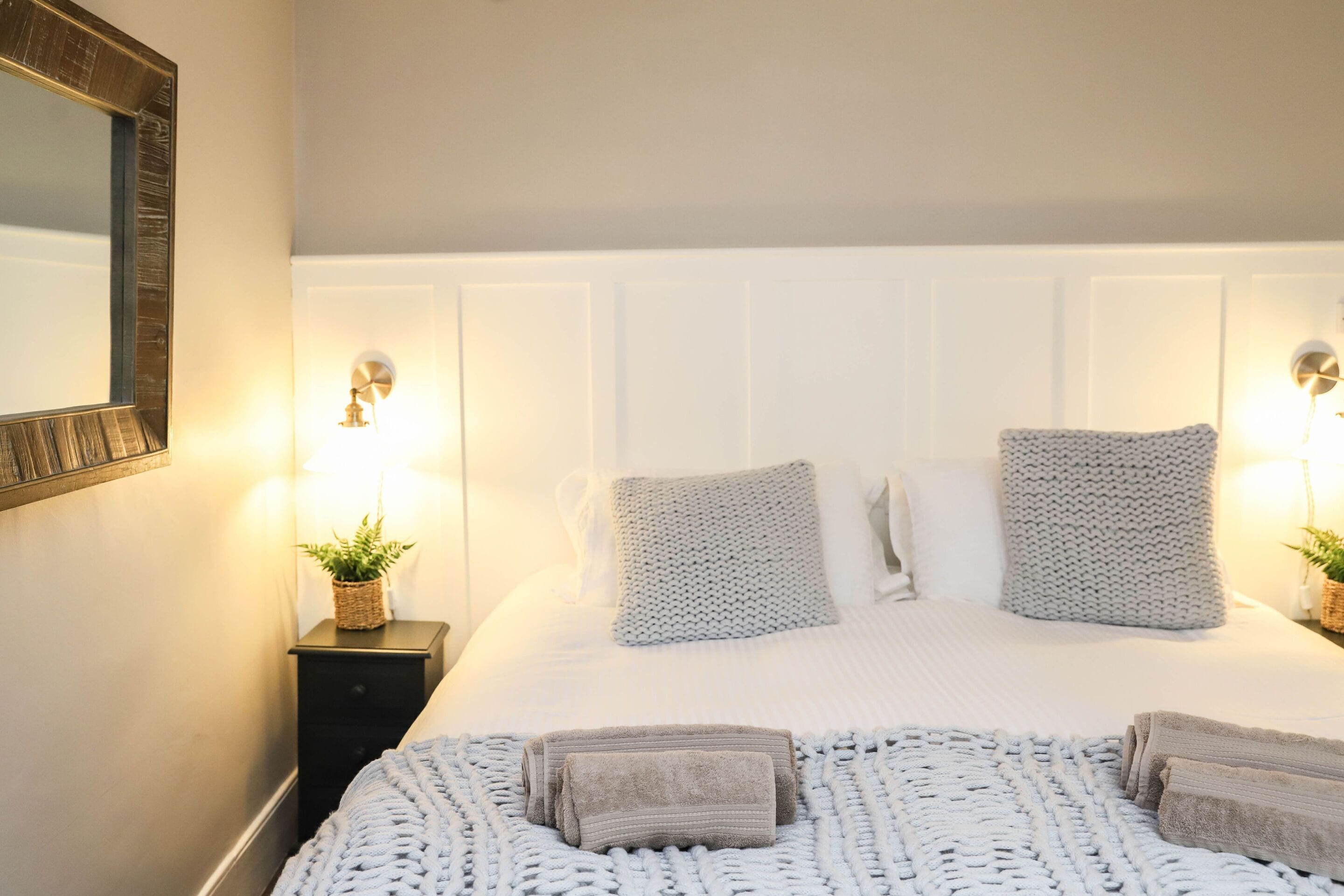 A neatly made bed with a white headboard, two bedside lamps, and a small plant on a nightstand.