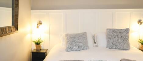 A neatly made bed with a white headboard, two bedside lamps, and a small plant on a nightstand.
