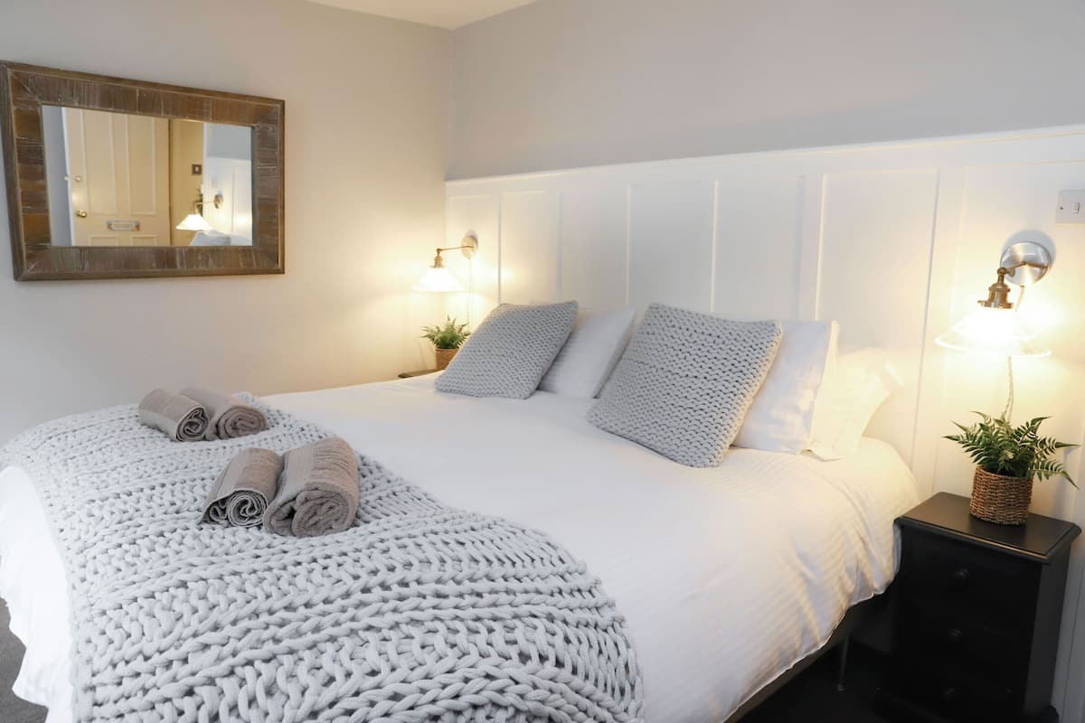 A neatly made bed with a white comforter and a knitted throw blanket, two bedside lamps, and a small potted plant on a nightstand.