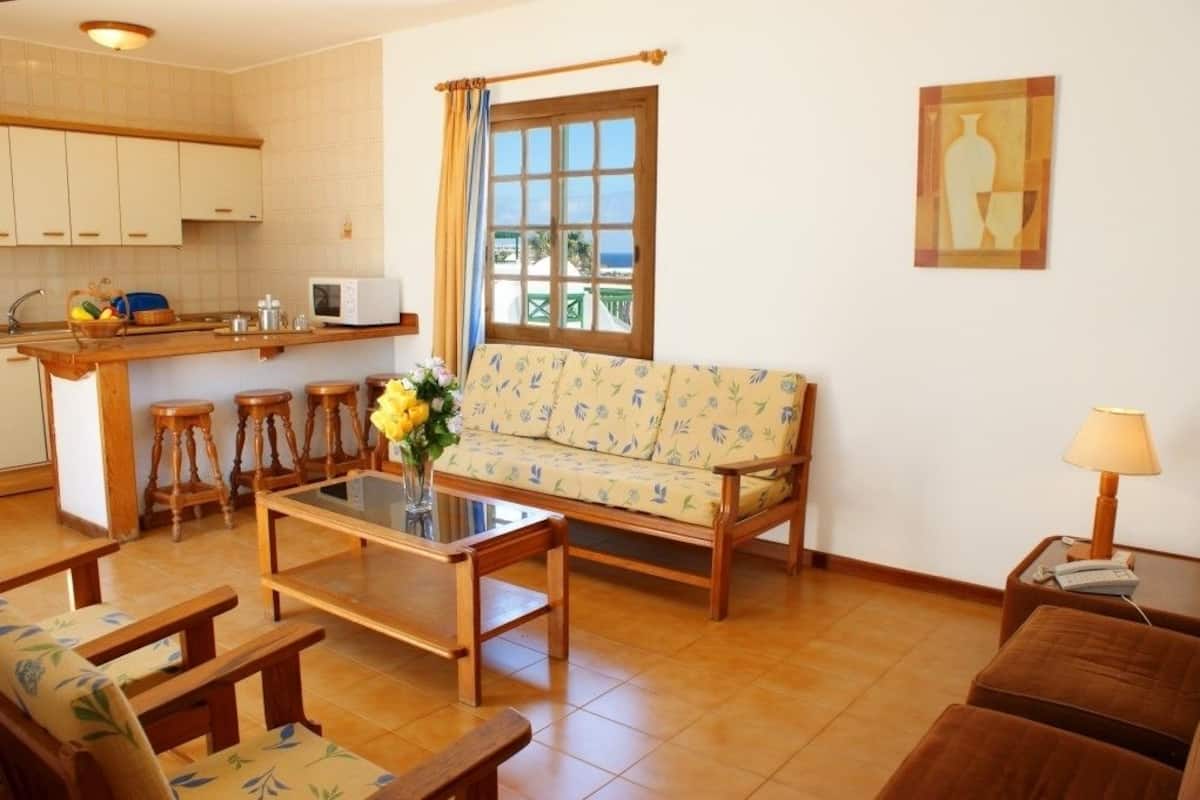 A compact living space with a sofa, coffee table, and bar stools in the living area, a kitchen with a microwave, and a window with a view.