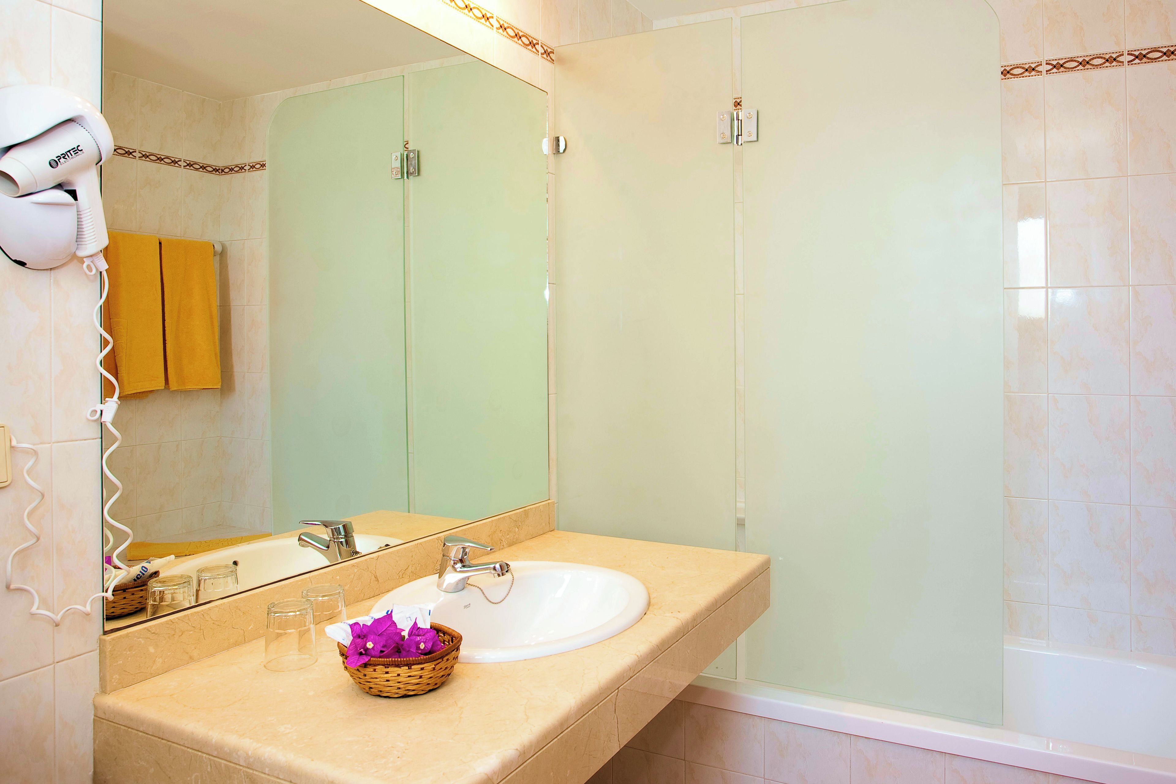 Un baño con un lavamanos blanco, un espejo, un perchero para toallas y una cabina de ducha.