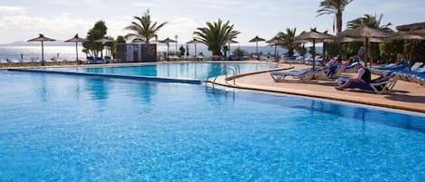 Une piscine d’un bleu éclatant, bordée de chaises longues et d’ombrelles, entourée de palmiers et offrant une vue sur la mer.