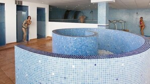 A modern indoor swimming pool with a tiled design, a central water feature, and a glass-enclosed area. - Monéa Royal Mónica (Yaiza)