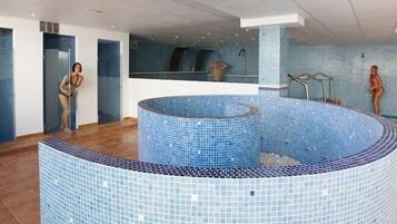 Una piscina interior moderna con diseño de azulejos, un elemento central de agua y una zona con cerramiento de vidrio.