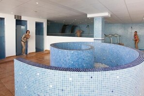 A modern indoor swimming pool with a tiled design, a central water feature, and a glass-enclosed area. - Monéa Royal Mónica (Yaiza)