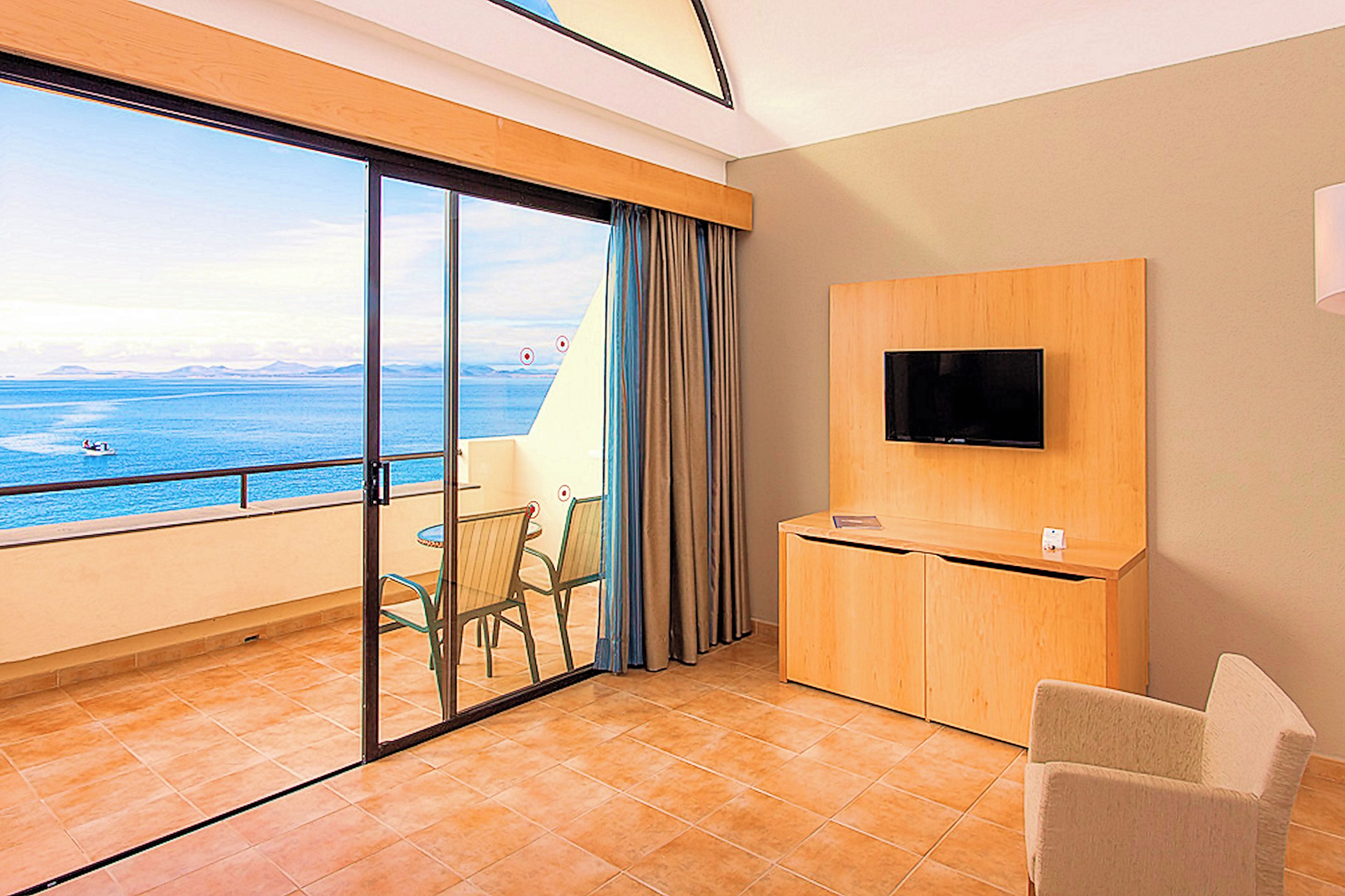 Ein Hotelzimmer mit Balkon, einem Wandfernseher, einem kleinen Schreibtisch und einem Stuhl.