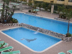 A swimming pool with a stone border, surrounded by lounge chairs and palm trees.