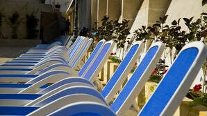Une rangée de chaises longues avec des coussins bleus, alignées le long d’un mur extérieur d’un bâtiment.