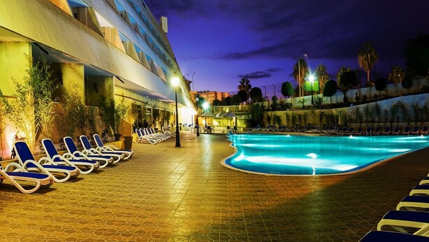 Un espace piscine d’hôtel avec des chaises longues et une lune dans le ciel.