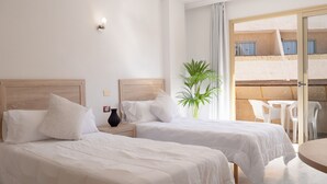 Une chambre d’hôtel avec deux lits, une plante en pot, une petite table et un balcon avec des chaises en plastique.