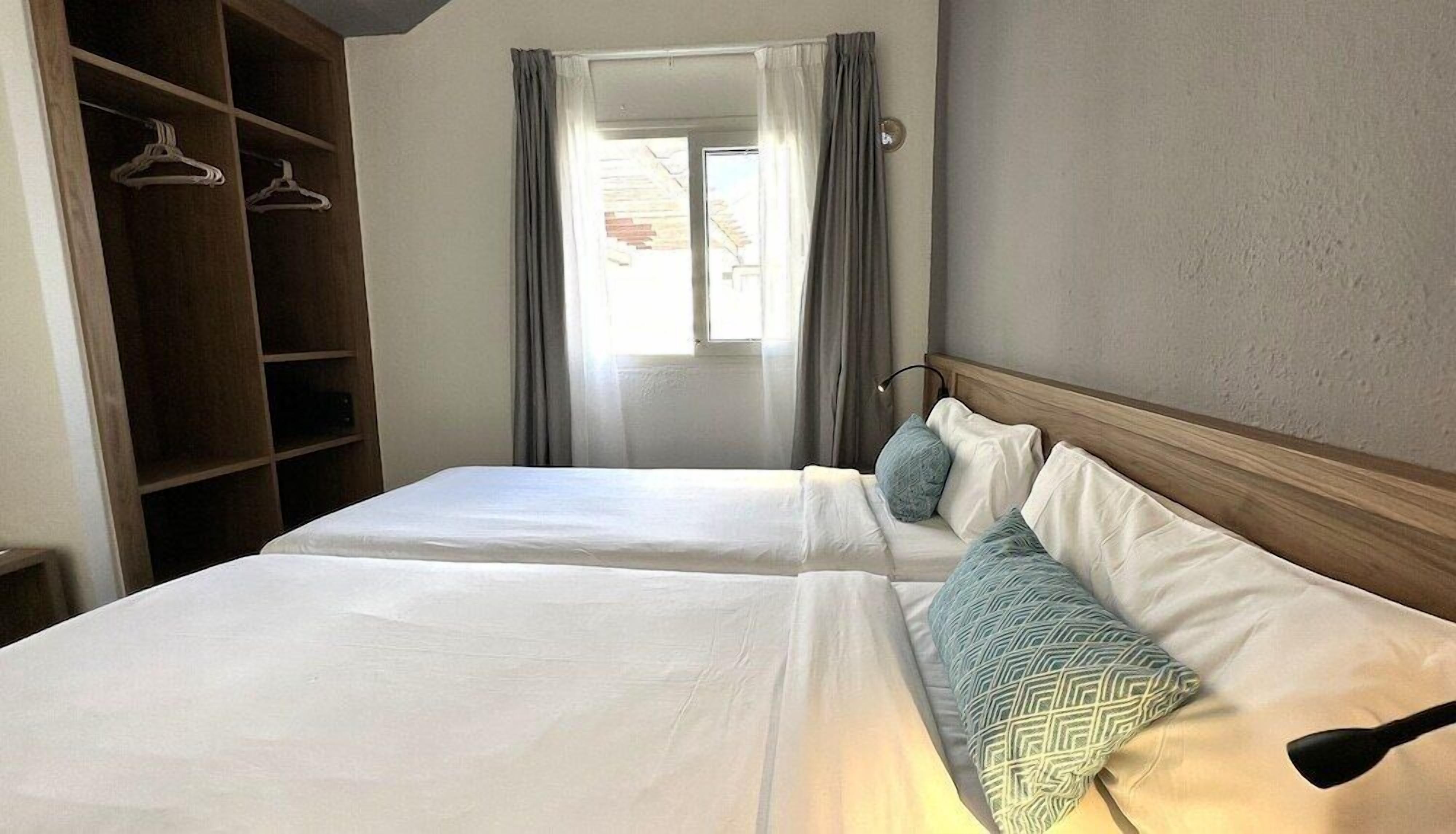 A hotel room with two beds, a wardrobe, and a window with curtains.