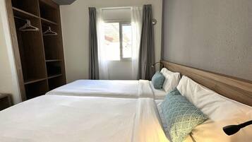 A hotel room with two beds, a wardrobe, and a window with curtains.