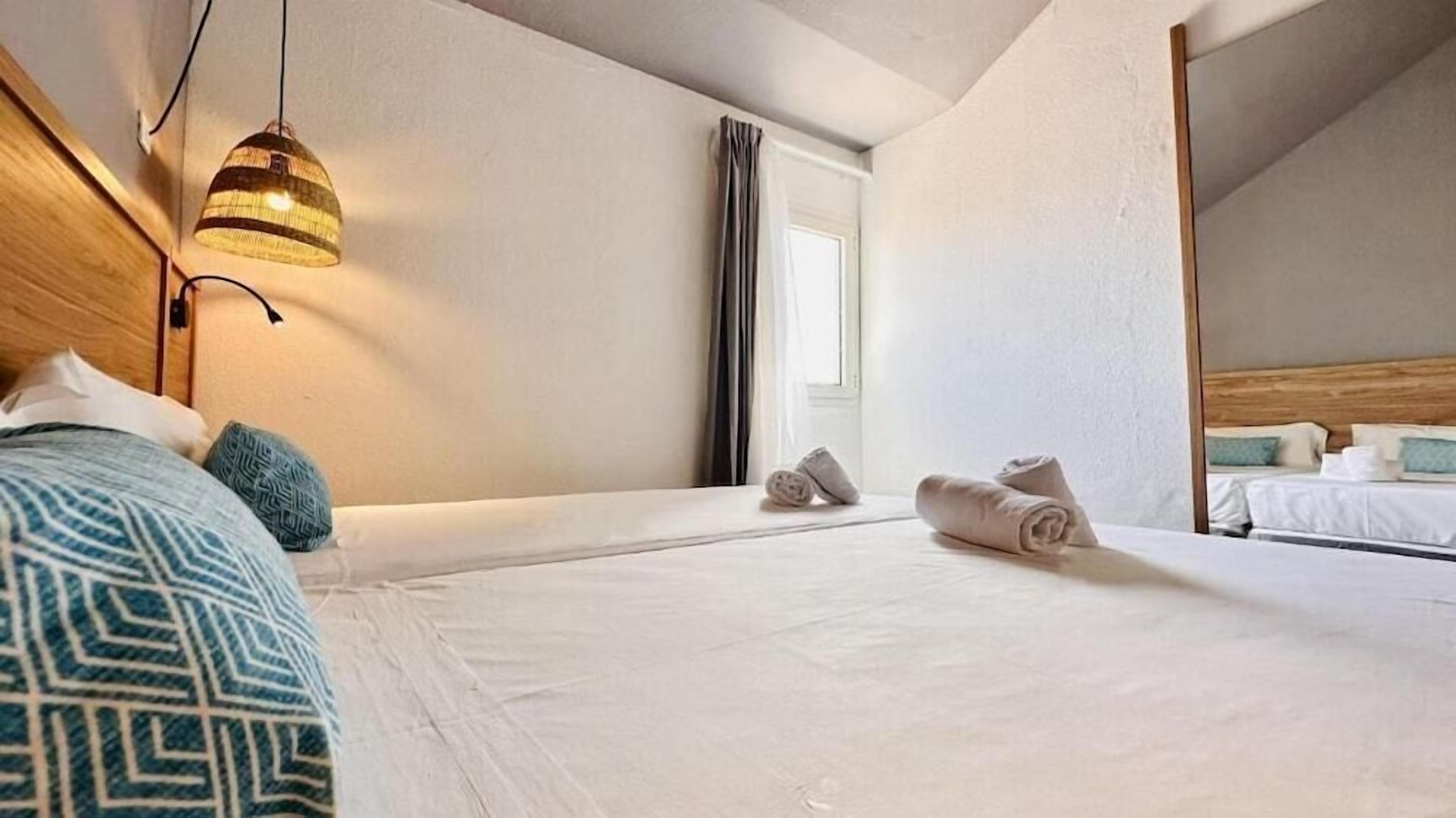 A hotel room with a large bed, a hanging light fixture, and a view of another room.