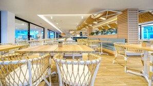 A modern dining area with wicker chairs and wooden tables, large windows, and a view of the cityscape. - Broncemar Beach (Antigua)