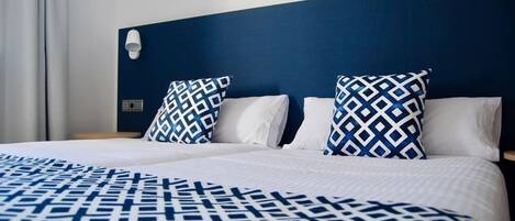 A hotel room with a large bed, two patterned pillows, a white headboard, and a nightstand with a lamp.