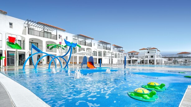 A swimming pool with water slides and a play area, surrounded by white buildings with balconies. - Broncemar Beach (Antigua)