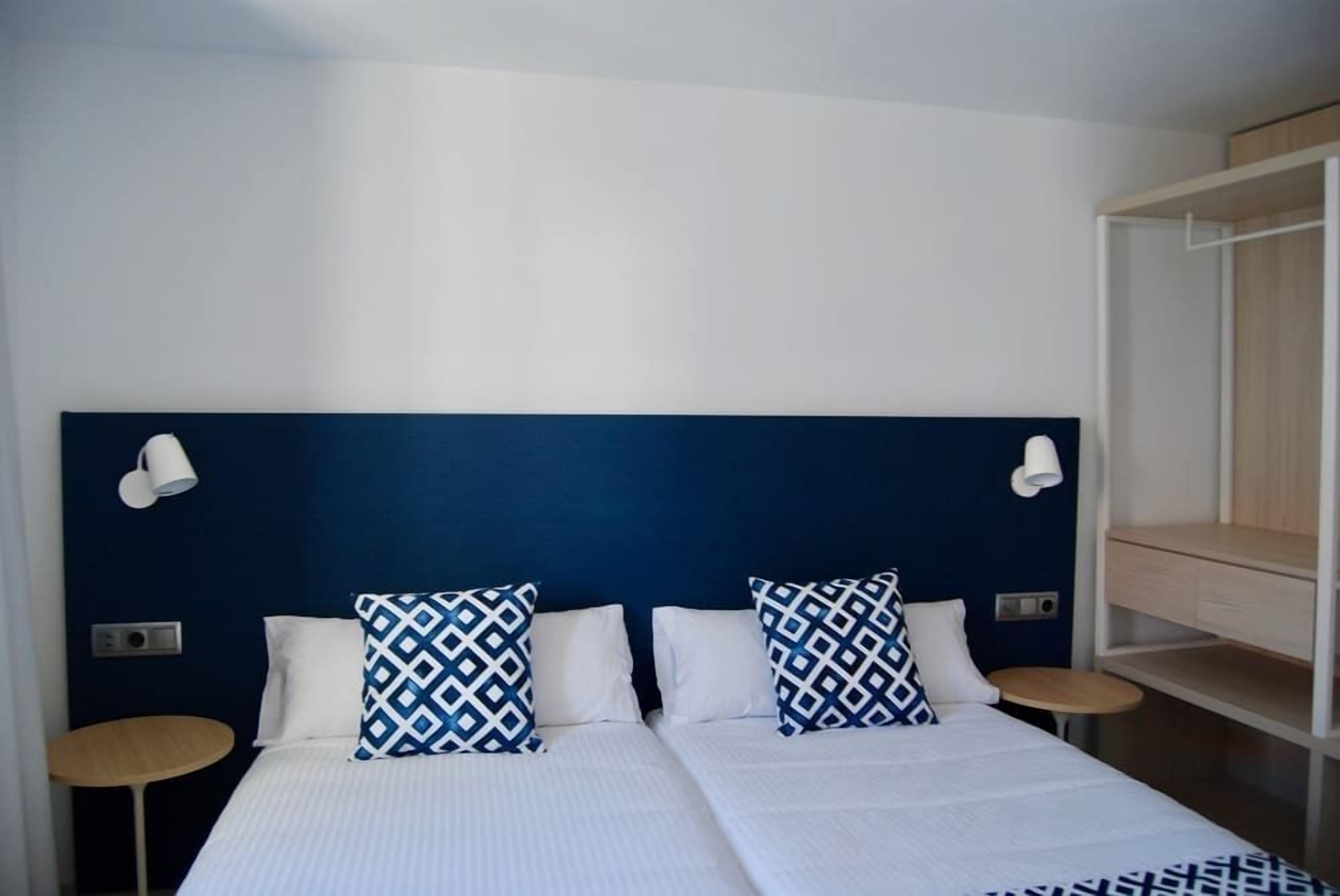 A double bed with white and blue patterned pillows, a dark blue headboard, and two bedside tables with lamps.
