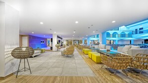 A spacious lobby with modern wicker furniture, a central seating area, and a view of a blue-lit upper level. - Broncemar Beach (Antigua)