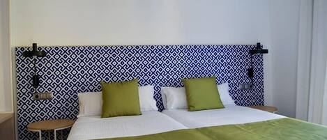A hotel room with a patterned headboard, a bed with white bedding and green pillows, and a small round table.