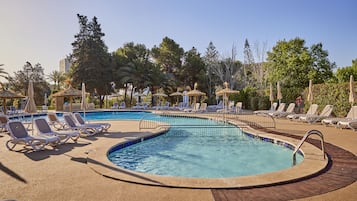 Un espace piscine agrémenté de chaises longues et de parasols, entouré d’arbres et d’immeubles.