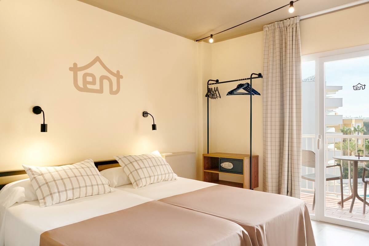 A hotel room with a bed, a wardrobe, a hanging clothes rack, and a view of the outside balcony.
