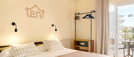 A hotel room with a bed, a wardrobe, a hanging clothes rack, and a view of the outside balcony.