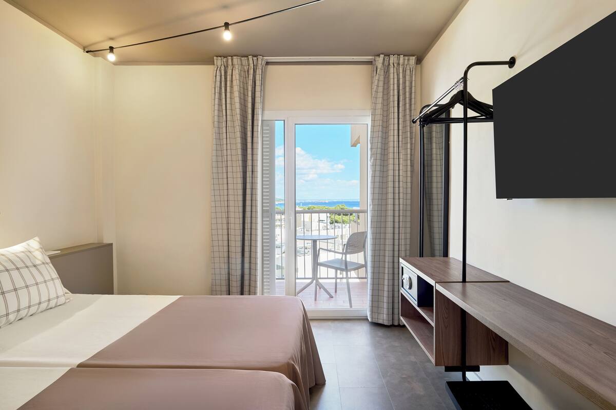 A hotel room with two beds, a desk, a TV, and a balcony with a view.