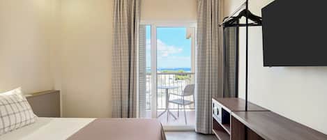 Habitación de hotel con dos camas, un escritorio, televisión y balcón con vistas.