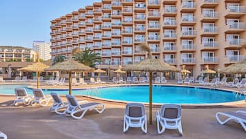A hotel pool area with lounge chairs and umbrellas, a large building with balconies in the background.