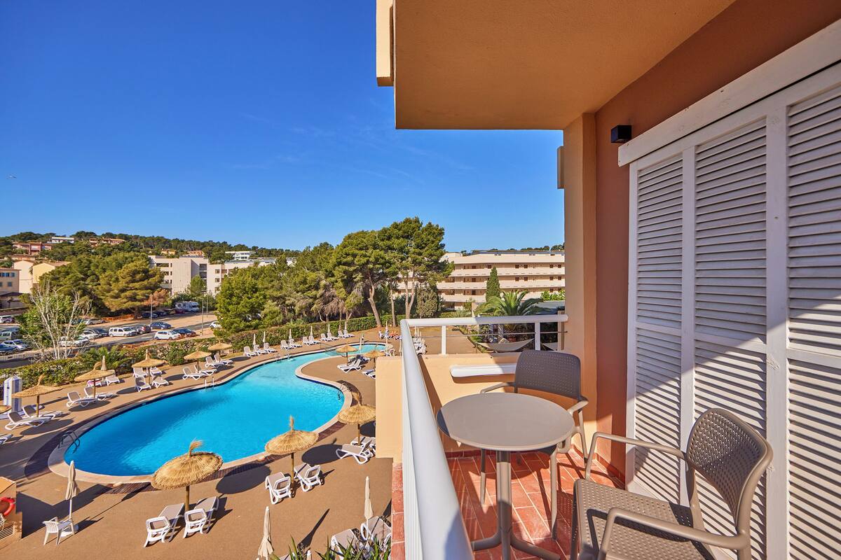 A balcony with a view of a swimming pool, lounge chairs, and a table.