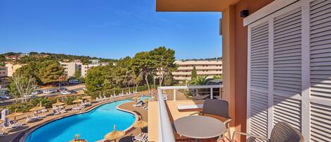 A balcony with a view of a swimming pool, lounge chairs, and a table.