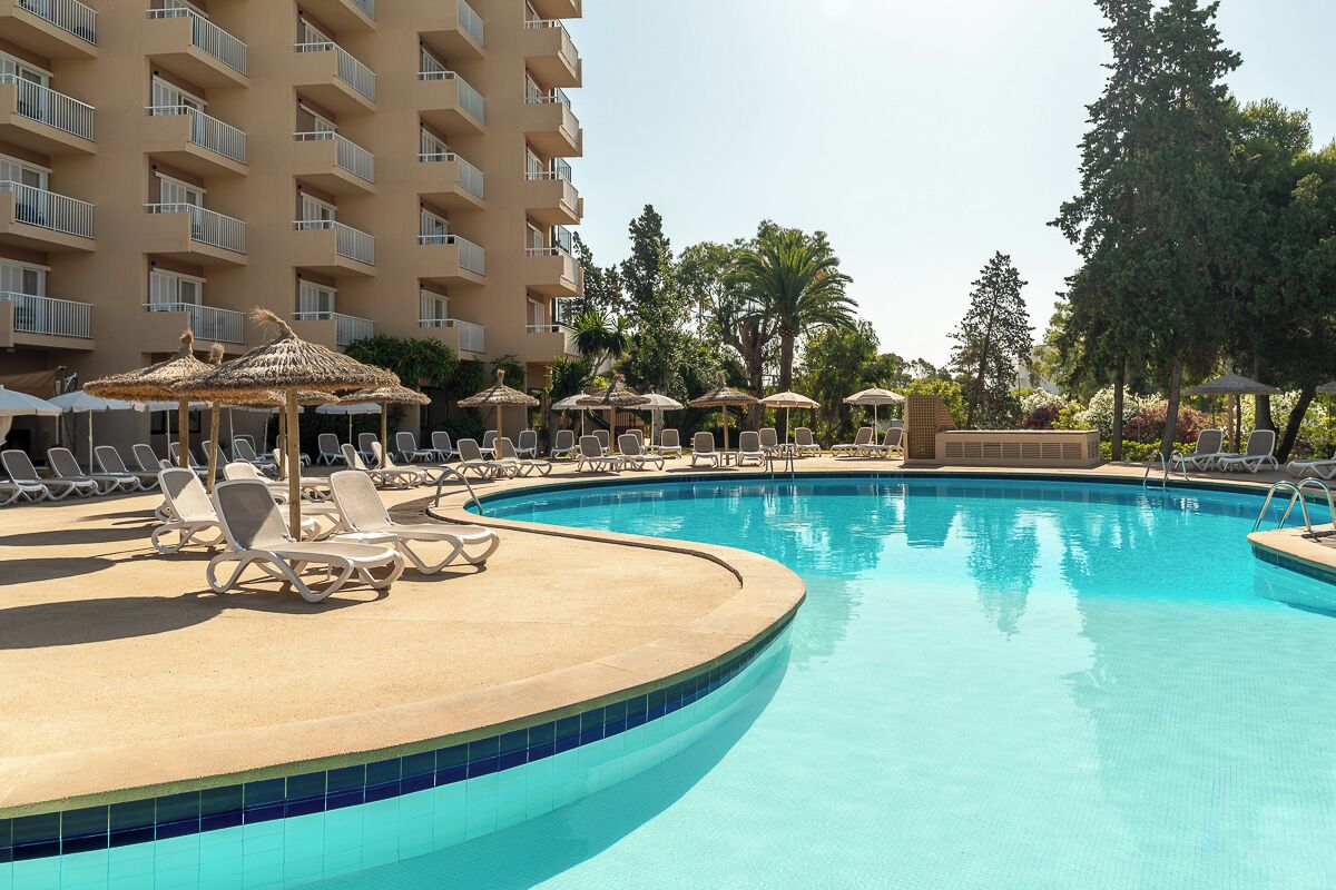 A swimming pool with lounge chairs and umbrellas, surrounded by a building with balconies.