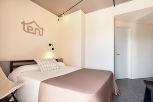 A modern hotel room with a neatly made bed, a wall-mounted light, and a door leading to another room.