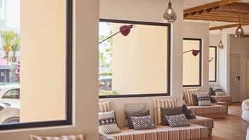 A modern interior with striped sofas and patterned cushions, large windows with views of the street, and pendant lighting.