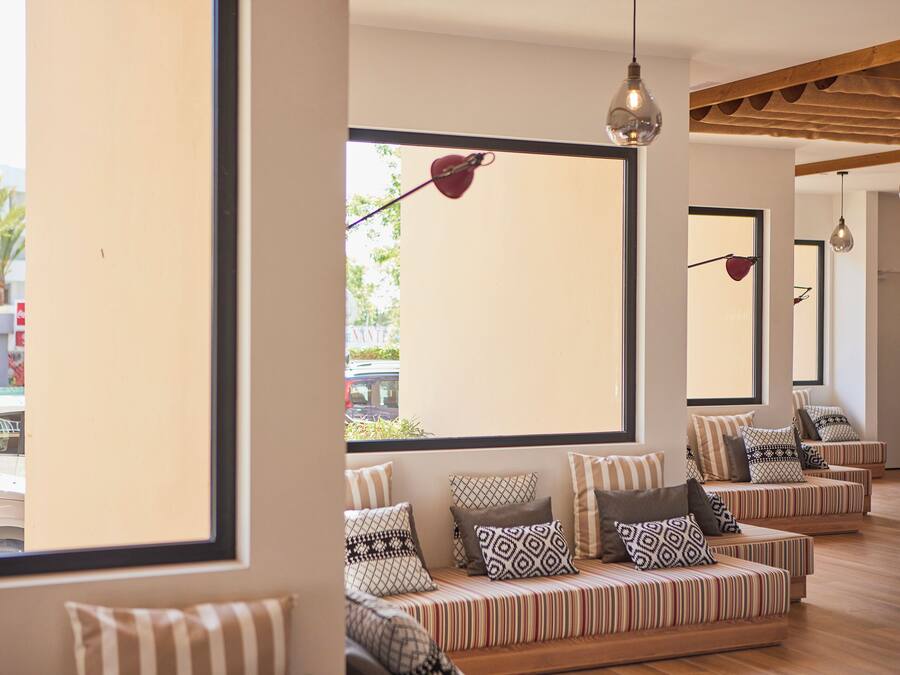 A modern interior with striped sofas and patterned cushions, large windows with views of the street, and pendant lighting.