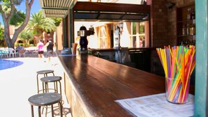 Un espace bar avec un comptoir en bois, des tabourets et un présentoir coloré rempli de pailles.