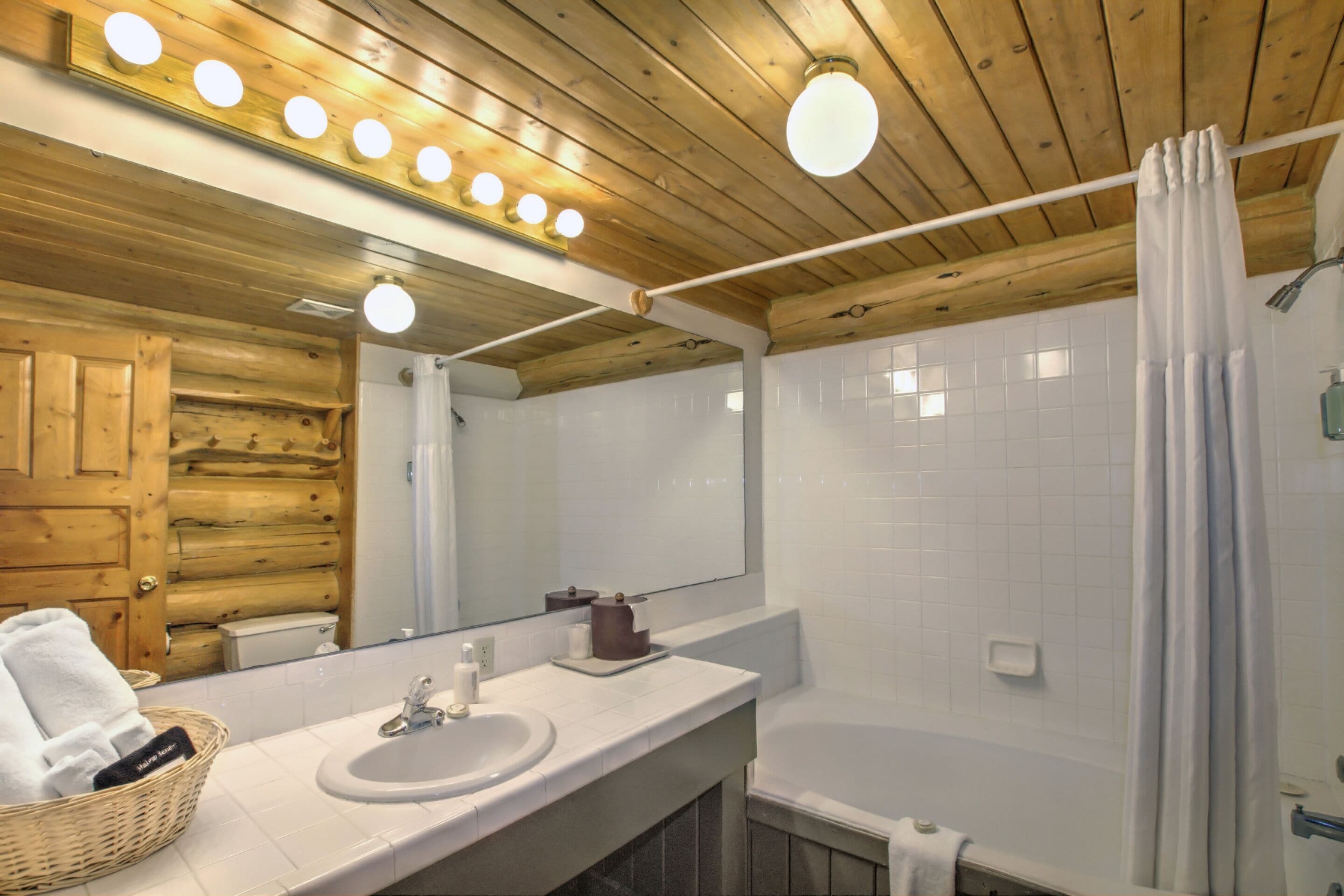 A bathroom with wooden ceiling, a white sink, a mirror, and a bathtub.