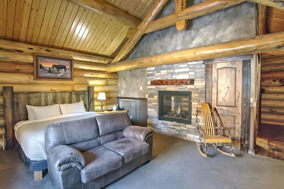 L’intérieur d’une cabane en rondins, avec un lit, un canapé en cuir, une cheminée et un plafond en bois rustique.
