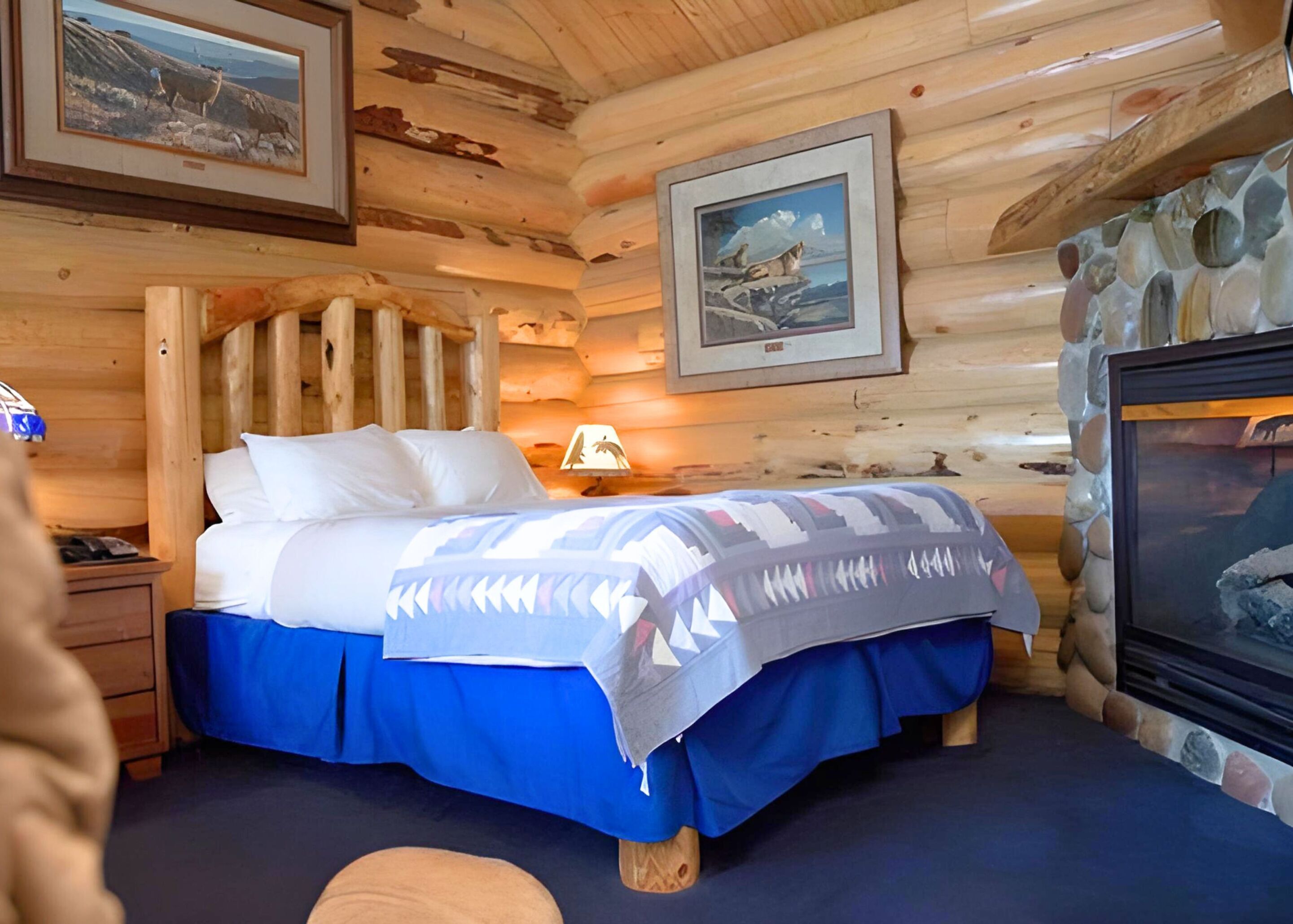 A cozy log cabin bedroom with a bed, a nightstand, a lamp, and framed pictures on the walls.