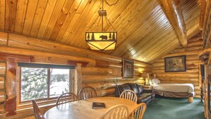 L’intérieur d’une cabane en rondins, avec une table à manger en bois, des chaises, un canapé et un lit.