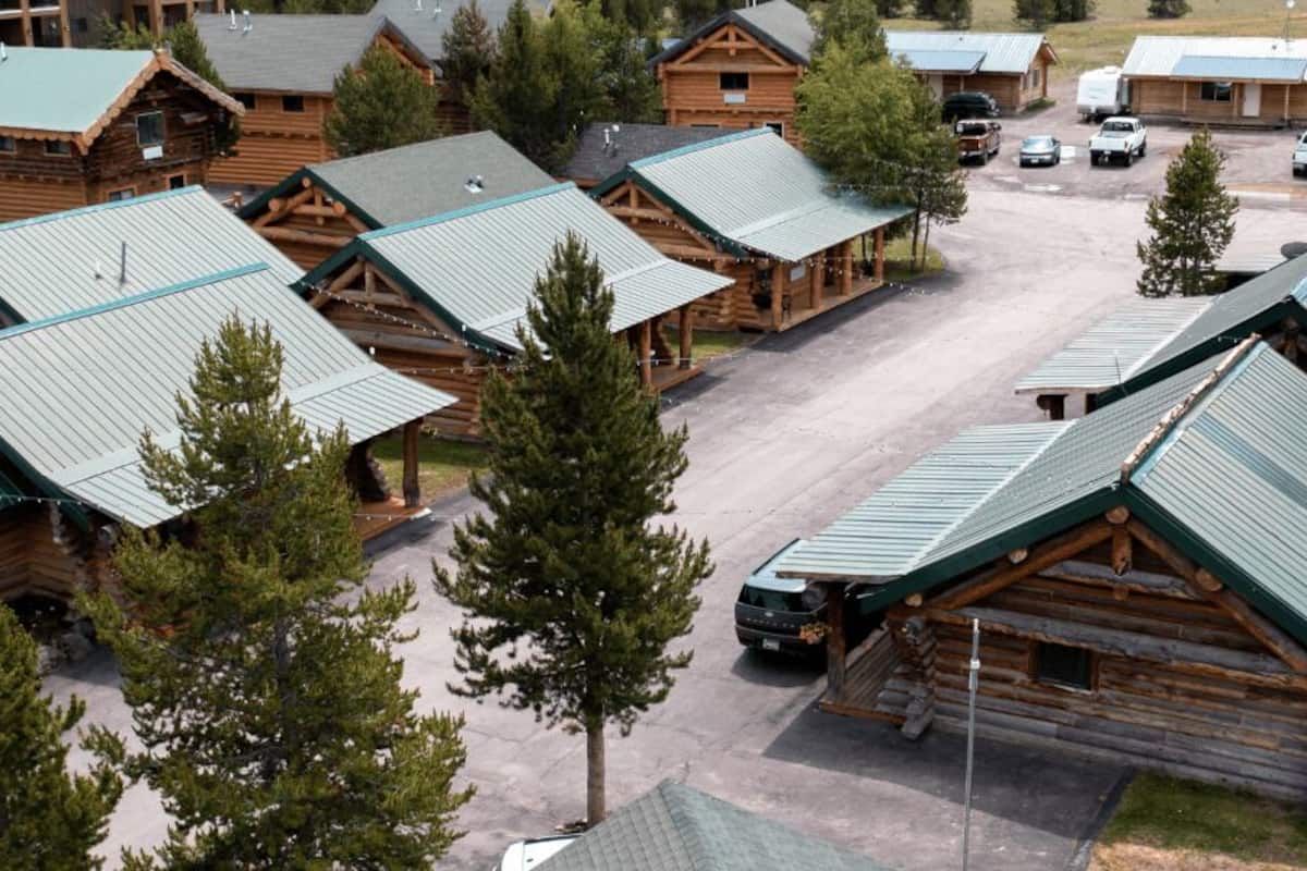 Un ensemble de chalets en rondins surmontés de toits métalliques, disposés en rangée avec un espace de stationnement devant.