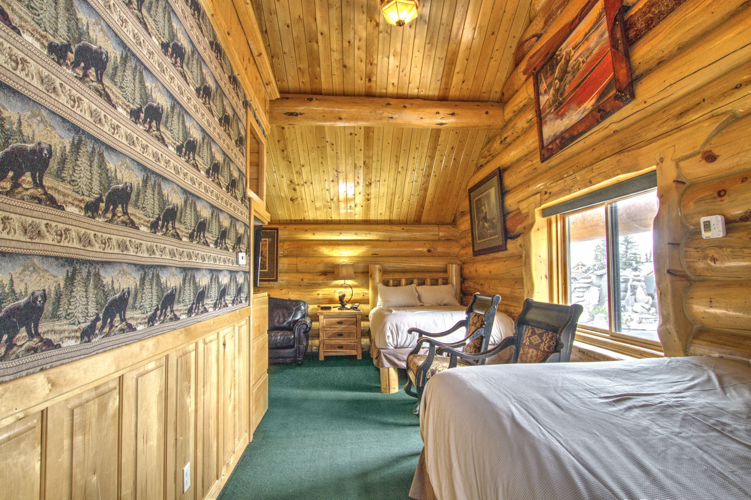 Une chambre aménagée dans un chalet en rondins, avec un lit, deux chaises, une table de chevet et une fresque murale représentant des ours.