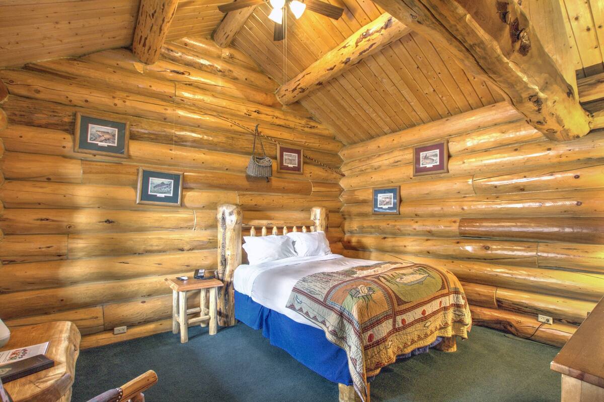 Une chambre à coucher dans un chalet en rondins, avec un lit en bois, une petite table de chevet et des tableaux encadrés accrochés aux murs.